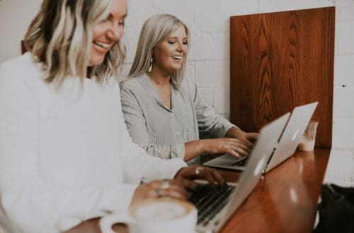 two women laughing and typing on a computer happy about work